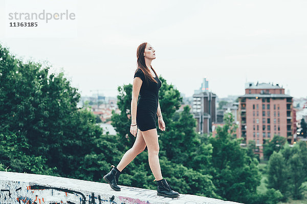 Junge Frau im Minikleid auf der Mauer über der Stadt spazierend