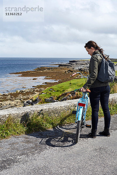 Junge Frau steht mit dem Fahrrad an der Seemauer  Inishmore  Irland