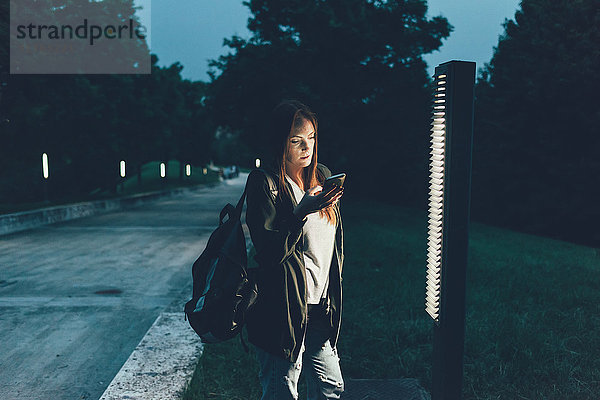 Junge Frau beim Lesen von Smartphone-Texten im Park bei Nacht