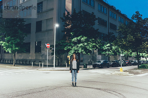 Porträt einer jungen Frau  die nachts an der Kreuzung der Stadt steht.