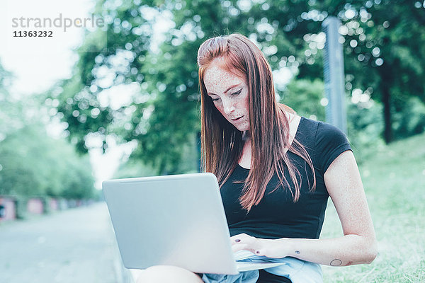 Junge Frau sitzt im Park und tippt auf dem Laptop