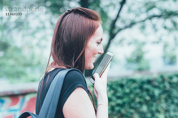 Junge Frau im Gespräch mit Smartphone im Park