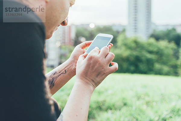 Abgeschnittene Aufnahme einer Frau auf Rasen mit Smartphone-Touchscreen