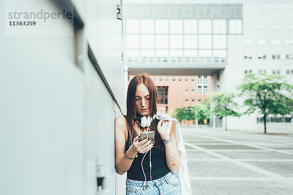 Junge Frau  die sich an die Wand lehnt und Smartphone-Texte liest.