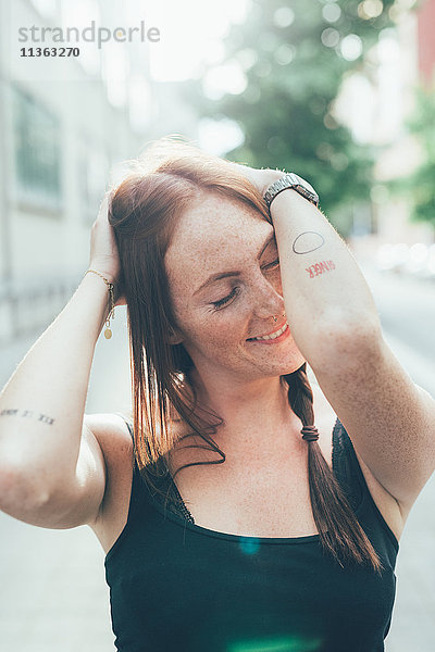 Junge Frau mit langen roten Haaren und Sommersprossen mit geschlossenen Augen auf der Stadtstraße