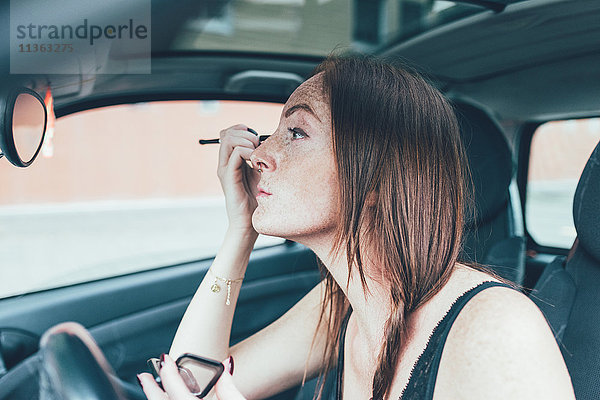 Junge Frau mit Sommersprossen mit Lidschatten im Autospiegel