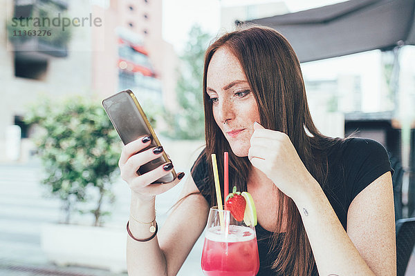 Junge Frau auf dem Bürgersteig Cafe lesen Smartphone-Texte