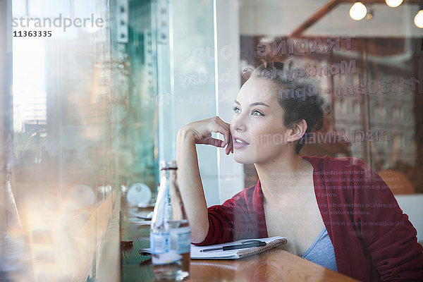 Junge Frau sitzt im Café und schaut aus dem Fenster