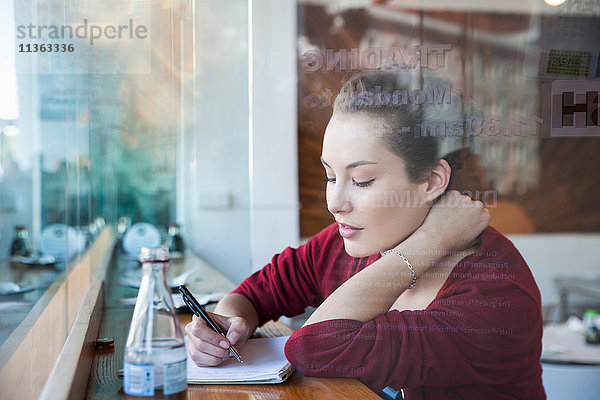 Junge Frau sitzt im Café und schreibt auf einem Notizblock