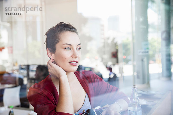 Junge Frau sitzt im Café und schaut aus dem Fenster
