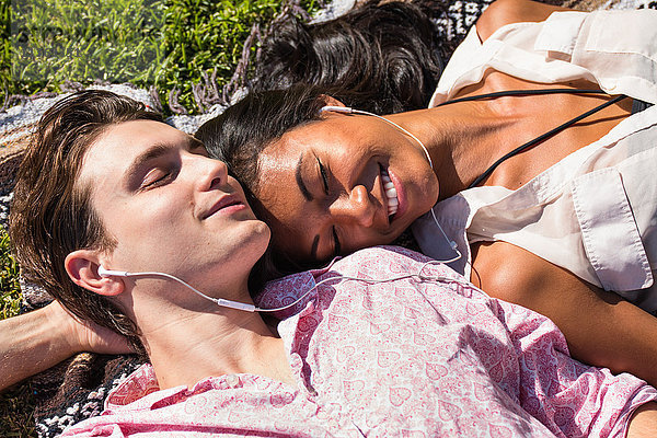 Junges Paar entspannt sich im Freien  liegt auf einer Decke im Gras und teilt sich Kopfhörer