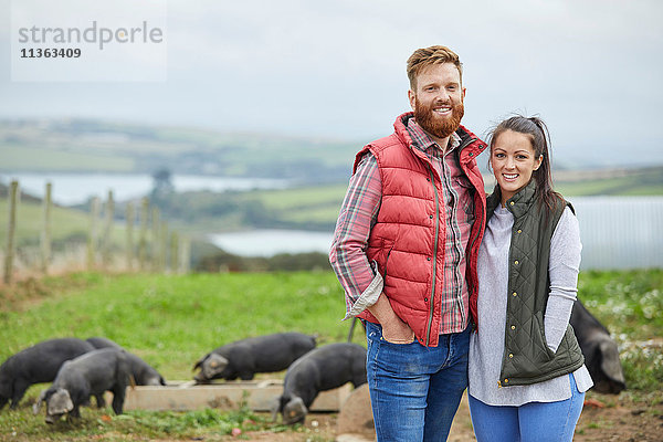 Ehepaar auf Schweinefarm schaut lächelnd in die Kamera