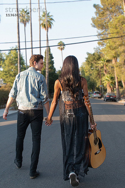 Junges Paar beim Spaziergang im Freien  junge Frau mit Gitarre in der Hand  Rückansicht