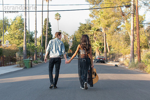 Junges Paar beim Spaziergang im Freien  junge Frau mit Gitarre in der Hand  Rückansicht