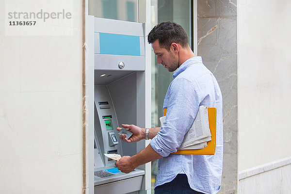 Mann beim Bargeldbezug am Geldautomaten