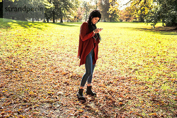 Junge Frau steht im Park und benutzt ein Smartphone