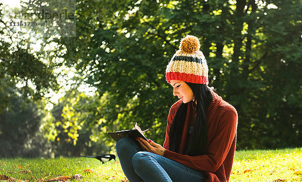Junge Frau sitzt auf Gras im Park und studiert