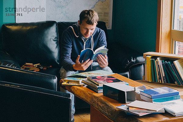 Mittelgroßer erwachsener Mann sitzt auf einem Stuhl und blättert in Büchern