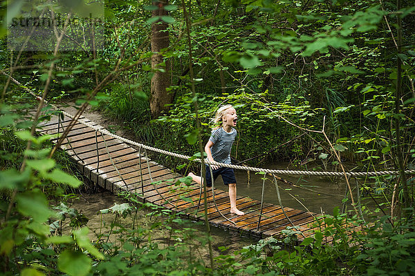 Junge läuft über eine Fussgänger-Seilbrücke im Wald