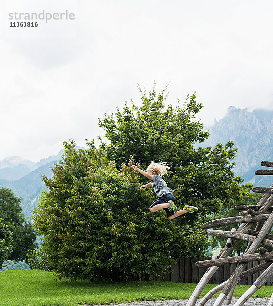 Junge in der Luft  der von einer Holzkonstruktion auf einem Spielplatz springt  Füssen  Bayern  Deutschland