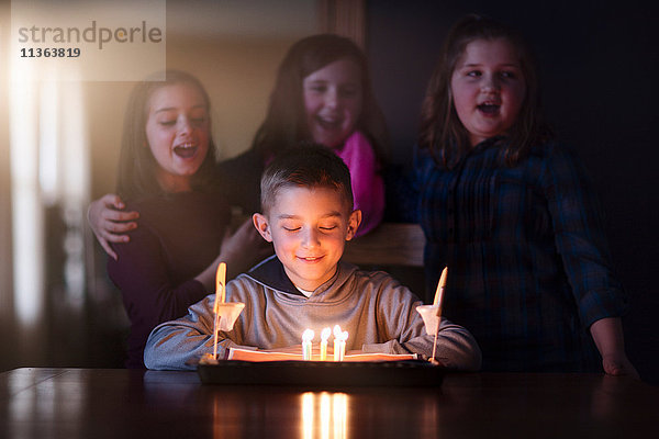 Junge von Freunden umgeben schaut lächelnd auf Geburtstagskuchen