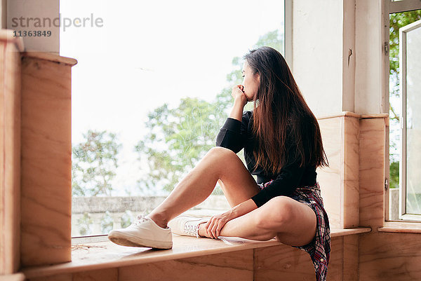 Junge Frau blickt vom Fensterbrett des verlassenen Hauses  Victoria Peak  Hongkong
