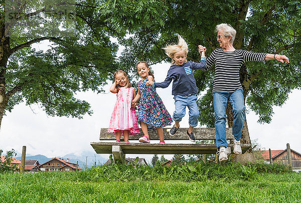 Großmutter und Enkelkinder in der Luft beim Sprung von der Parkbank  Füssen  Bayern  Deutschland