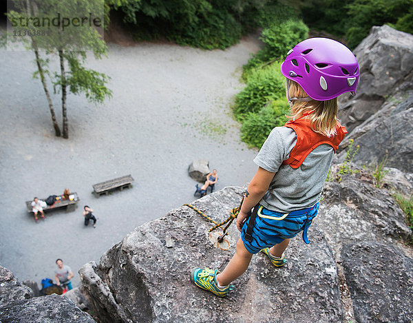 Junge mit Kletterhelm auf Fels stehend mit Blick nach unten