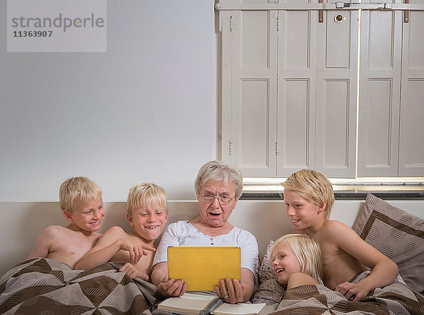 Großmutter im Bett mit Enkelkindern mit digitalem Tablett