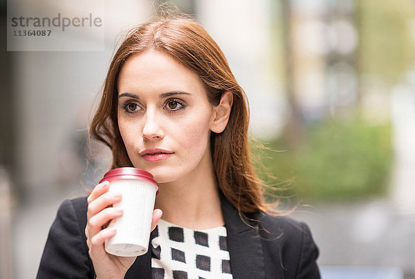 Porträt einer Frau  die eine Einweg-Kaffeetasse in der Hand hält und wegschaut.