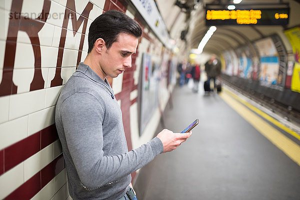 Seitenansicht des Mannes auf dem Bahnsteig mit Blick auf das Smartphone
