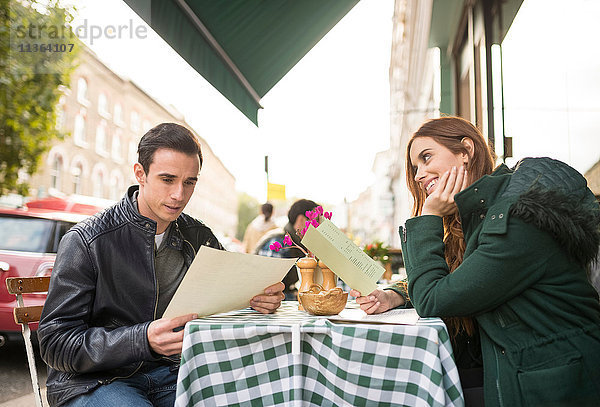 Paar im Straßencafé mit lächelndem Blick auf die Speisekarte