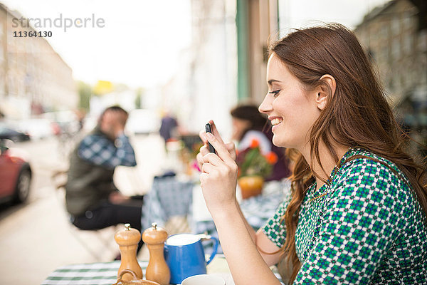Seitenansicht der Frau im Straßencafé mit Blick auf das lächelnde Smartphone