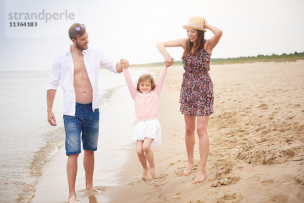 Familie geht am Strand spazieren und schwingt die Tochter mit der Hand