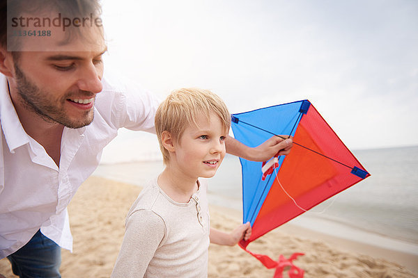 Vater und Sohn spielen Drachen am Strand