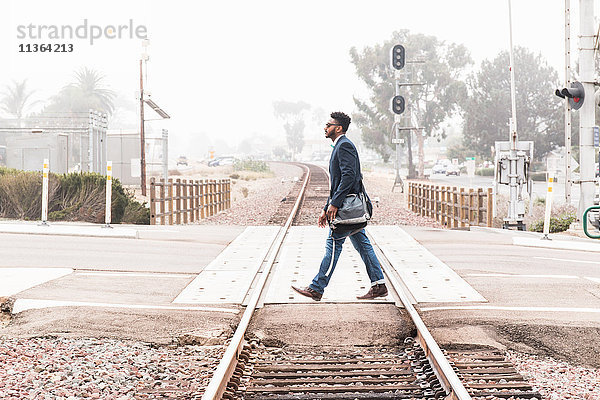 Junger Mann beim Überqueren eines Bahnübergangs  Seitenansicht