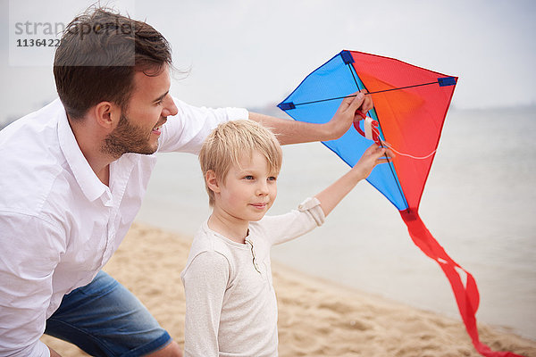 Vater und Sohn spielen Drachen am Strand