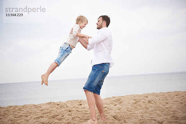 Vater schwingt Sohn am Strand