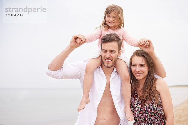 Familie geht am Strand spazieren  Tochter sitzt auf den Schultern des Vaters