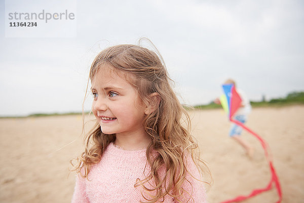 Kleines lächelndes Mädchen am Strand  Drachen spielende Person im Hintergrund