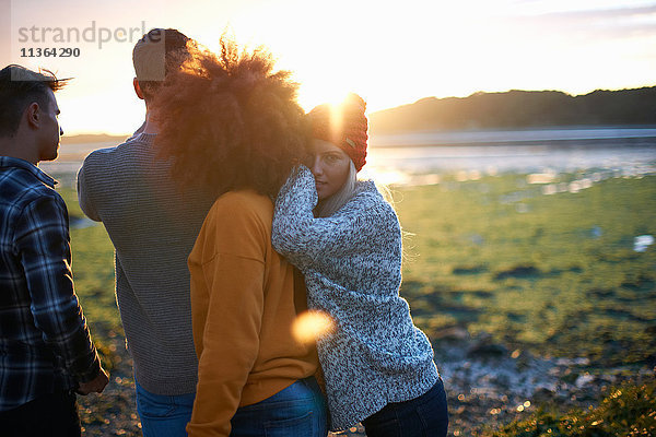 Porträt einer jungen Frau mit erwachsenen Freunden beim Sonnenuntergang über dem Meer