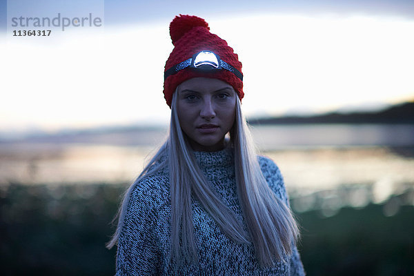 Porträt einer jungen Frau mit Stirnlampe auf See in der Abenddämmerung