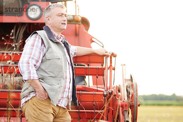 Landwirt lehnt sich an Mähdrescher an und schaut weg