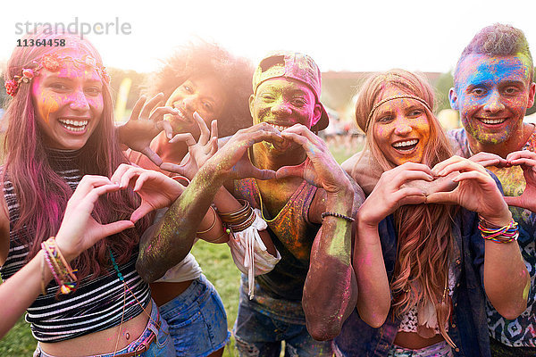 Porträt einer Gruppe von Freunden beim Festival  mit bunter Pulverfarbe überzogen  die mit den Händen Herzformen herstellt