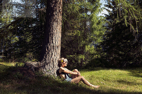 Mittlere erwachsene Frau  die sich an einen Waldbaumstamm lehnt  Sattelbergalm  Tirol  Österreich