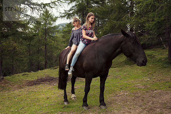 Mädchen und Frau sitzen ohne Sattel auf einem Pferd auf einer Waldlichtung  Sattelbergalm  Tirol  Österreich