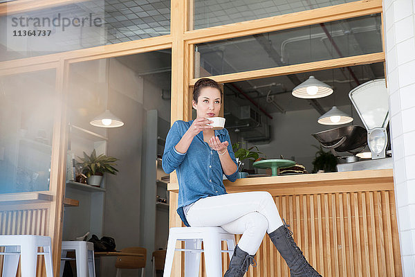 Junge Frau sitzt an der Bar im Café und hält eine Kaffeetasse