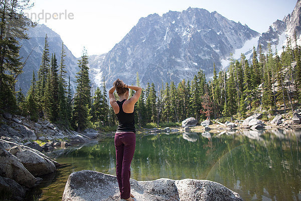 Junge Frau steht auf einem Felsen am See und schaut auf die Aussicht  Die Verzauberungen  Alpine Lakes Wilderness  Washington  USA