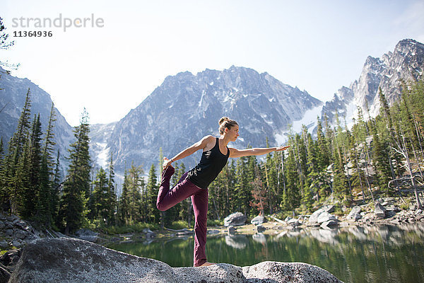 Junge Frau steht auf einem Felsen am See  in Yoga-Pose  Die Verzauberungen  Alpine Lakes Wilderness  Washington  USA