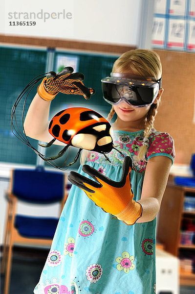 Mädchen  das sich als Lehrerin ausgibt und ein Virtual-Reality-Headset und Handschuhe trägt  um Marienkäfer zu zeigen